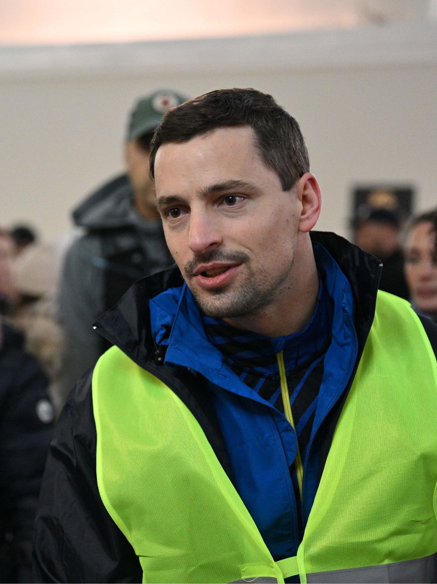 Bénévole en gilet jaune de sécurité, attentif au milieu de la foule en intérieur