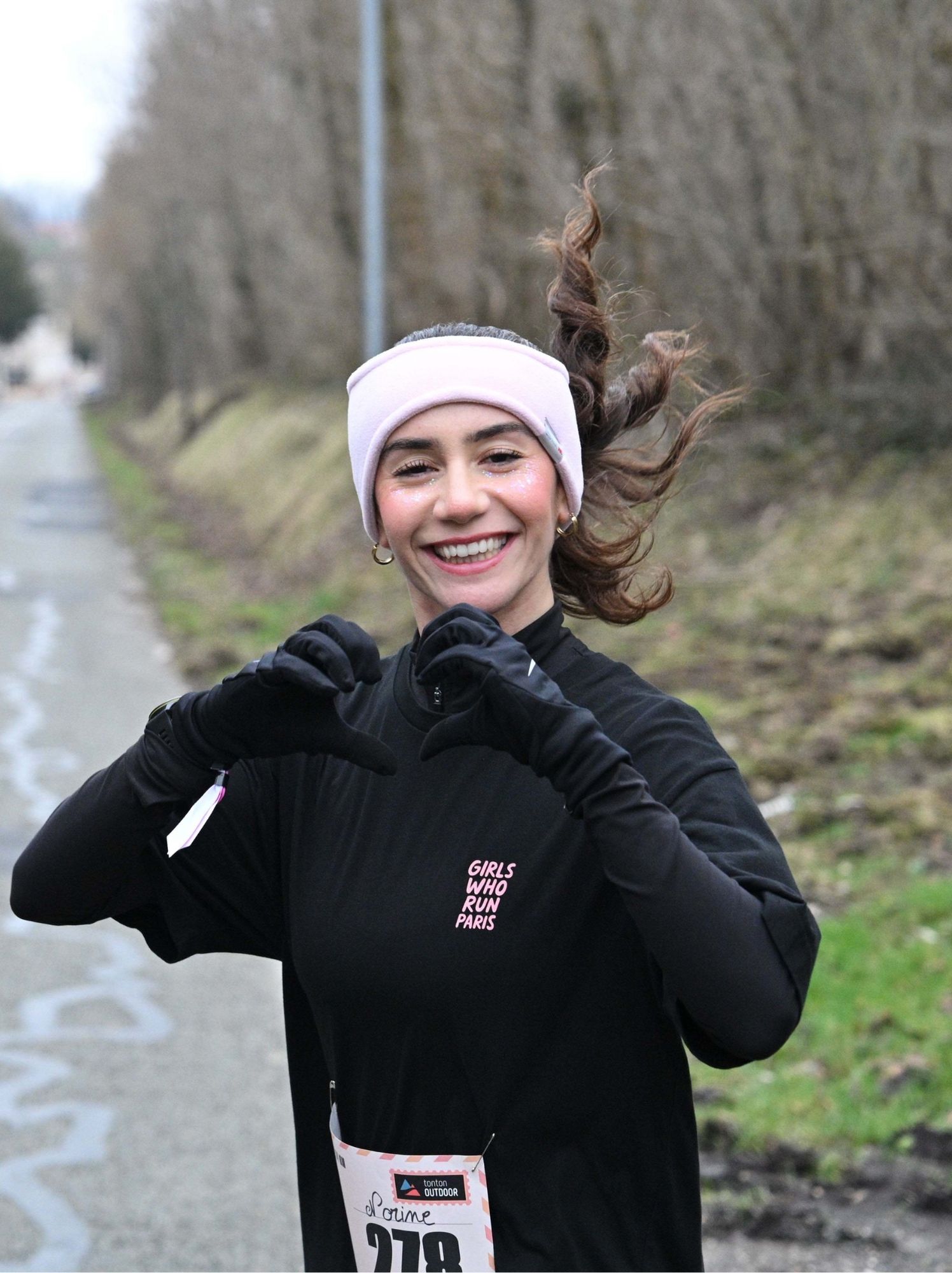 Coureuse formant un cœur de ses mains gantées en courant sur une route bordée de talus