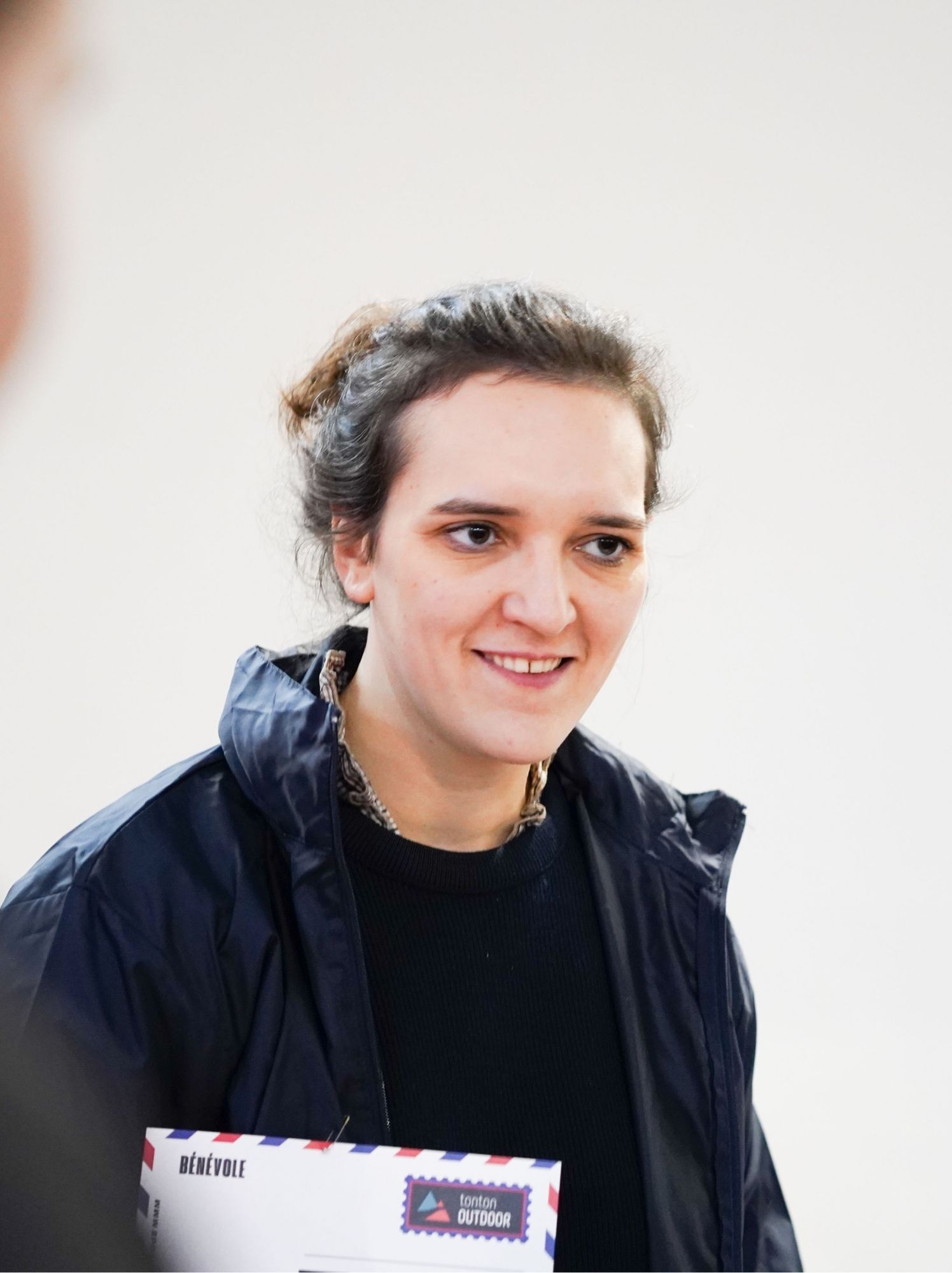 Bénévole souriante tenant son enveloppe de bénévole devant un mur clair