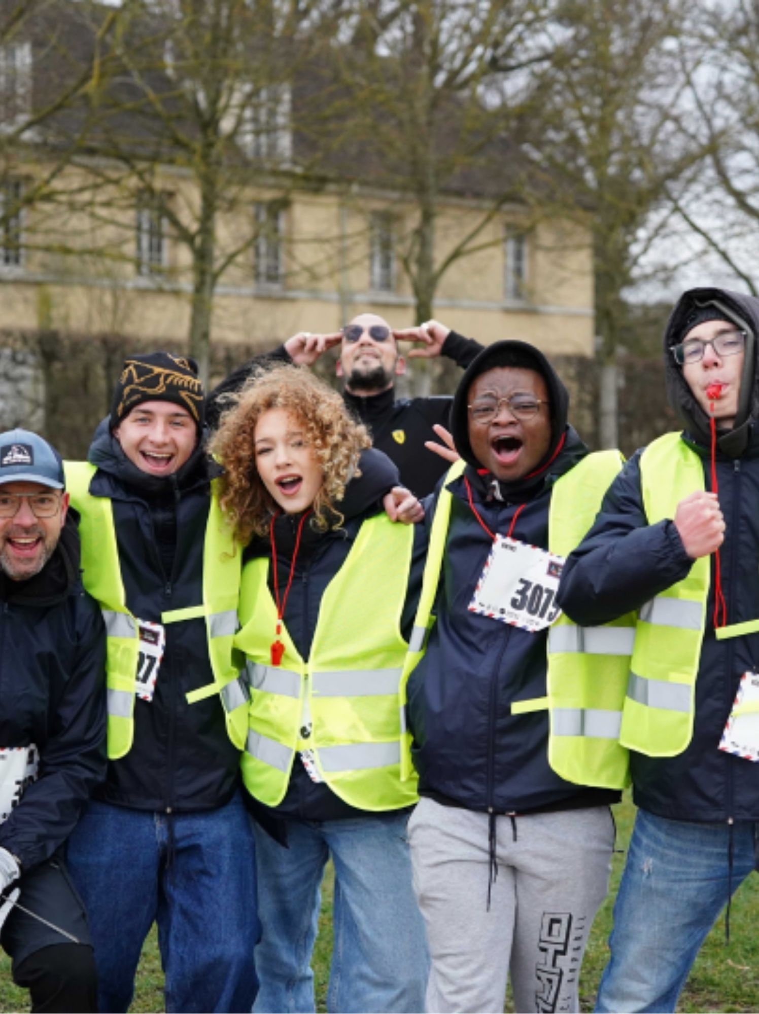 Équipe de bénévoles en gilets jaunes, bras dessus bras dessous, sifflant et riant ensemble
