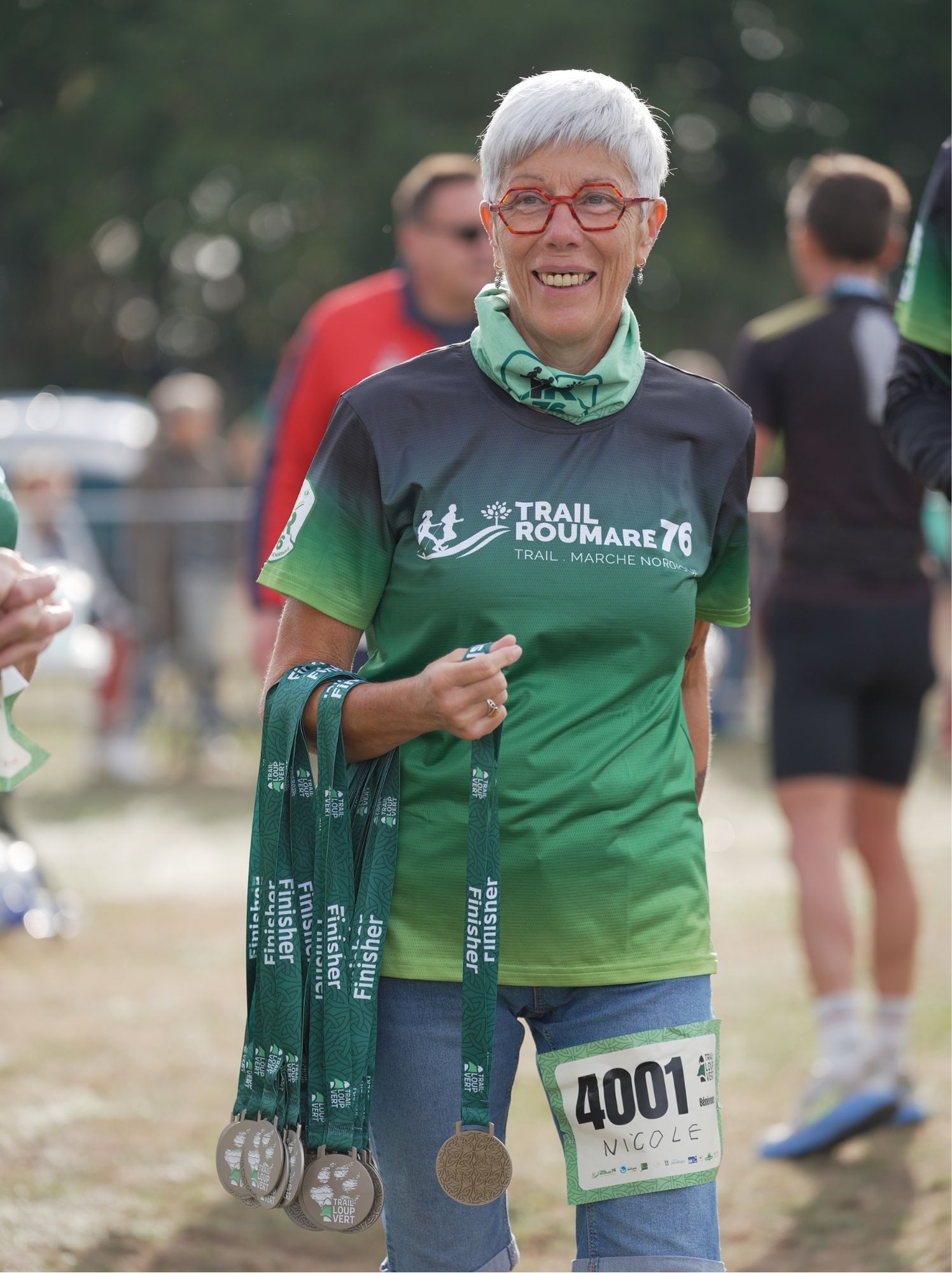 Bénévole souriante, les bras chargés de médailles finisher